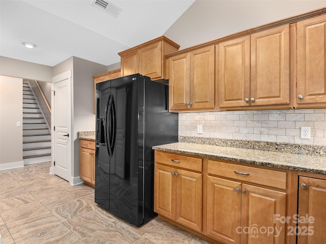 kitchen featuring decorative backsplash, black refrigerator with ice dispenser, and light stone counters