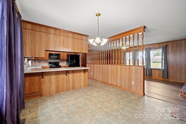 kitchen with light countertops, an inviting chandelier, wooden walls, a peninsula, and black appliances