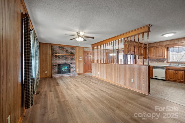 unfurnished living room featuring wooden walls, a fireplace, a sink, and light wood-style flooring