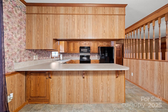 kitchen with a breakfast bar area, light countertops, a sink, a peninsula, and black appliances