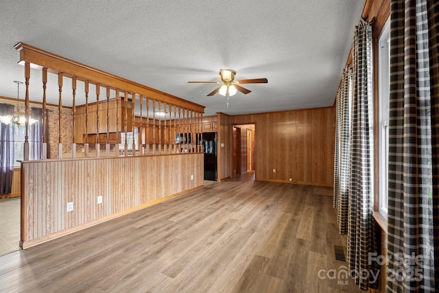 unfurnished living room featuring a textured ceiling, wood finished floors, and ceiling fan with notable chandelier