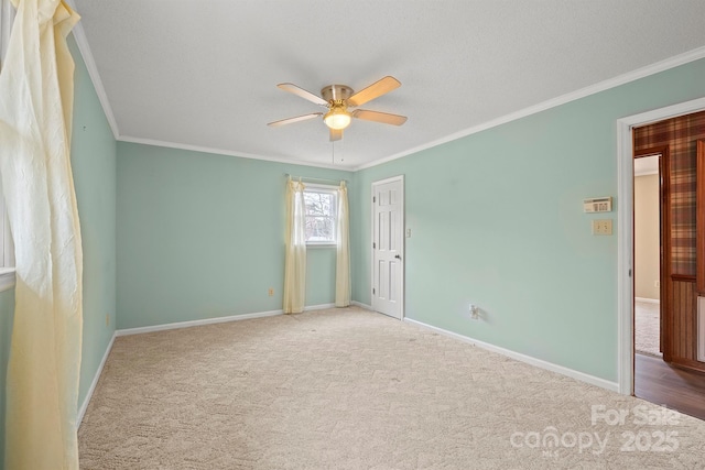 empty room with carpet floors, ornamental molding, a ceiling fan, and baseboards