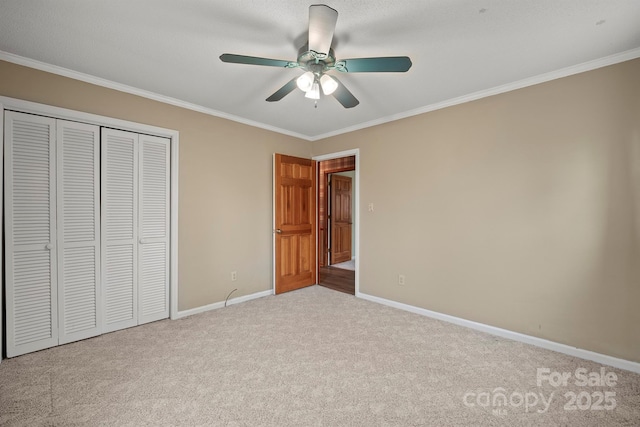 unfurnished bedroom featuring baseboards, a ceiling fan, ornamental molding, carpet flooring, and a closet