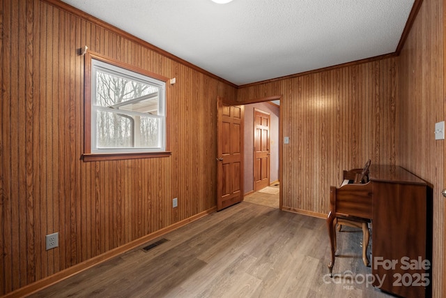 sitting room featuring wood walls, wood finished floors, visible vents, baseboards, and ornamental molding