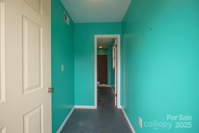 hallway with visible vents, concrete floors, and baseboards