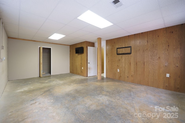 basement featuring wood walls, visible vents, and a drop ceiling