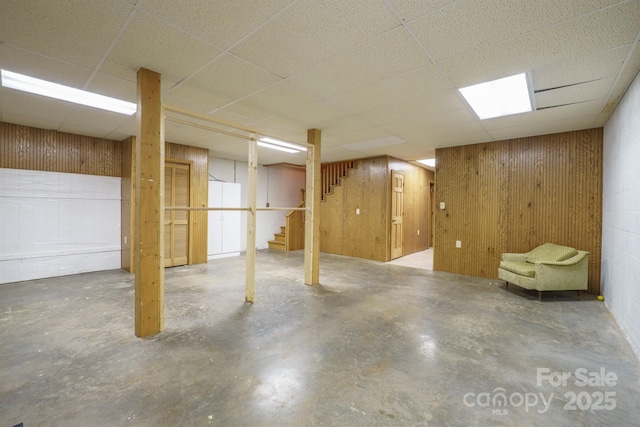 finished basement with stairs, wood walls, and a drop ceiling