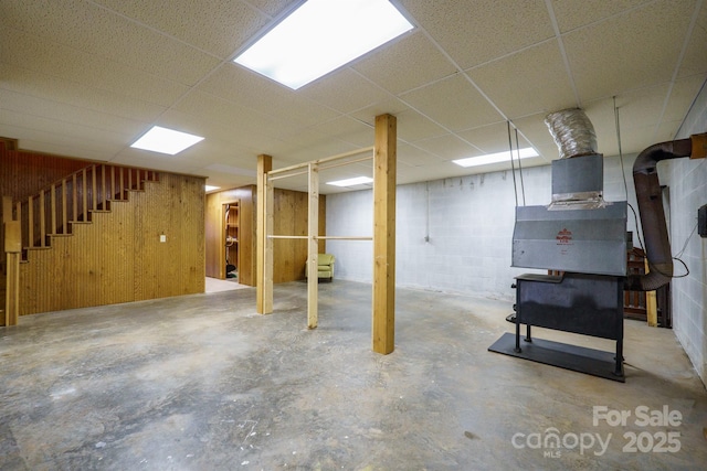 finished basement featuring concrete block wall, stairs, wooden walls, and a drop ceiling