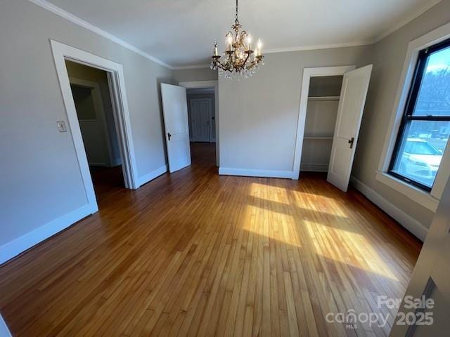 unfurnished bedroom with hardwood / wood-style flooring, crown molding, a closet, and a notable chandelier