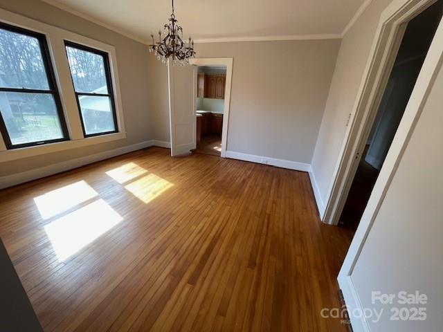 unfurnished dining area featuring an inviting chandelier, crown molding, and hardwood / wood-style floors