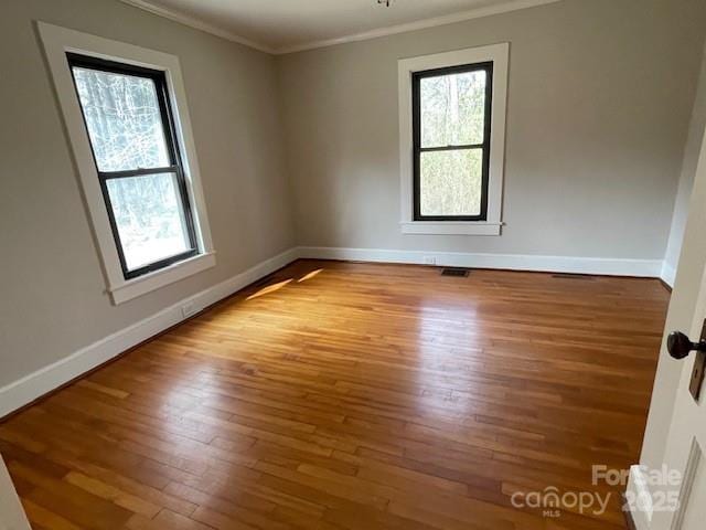 empty room featuring hardwood / wood-style flooring, a wealth of natural light, and ornamental molding