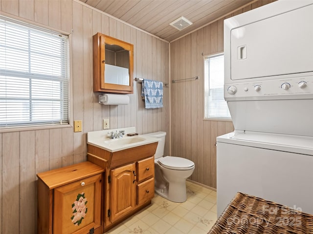 bathroom with toilet, wood walls, wooden ceiling, vanity, and stacked washer / dryer