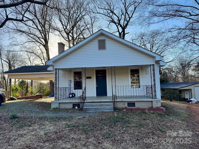 bungalow-style home featuring an attached carport, a chimney, covered porch, and crawl space