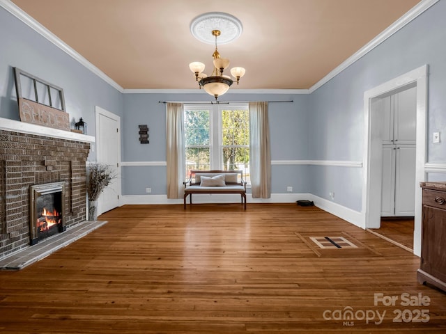 unfurnished dining area with ornamental molding, a brick fireplace, an inviting chandelier, and wood finished floors