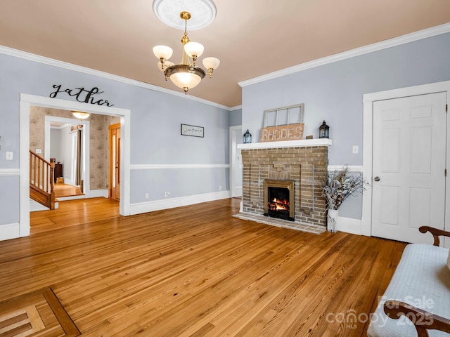 living room with a fireplace, wood finished floors, baseboards, ornamental molding, and an inviting chandelier