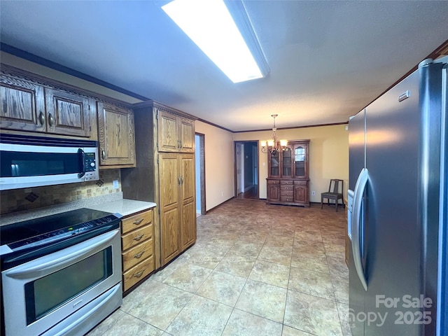 kitchen featuring light countertops, appliances with stainless steel finishes, backsplash, an inviting chandelier, and crown molding