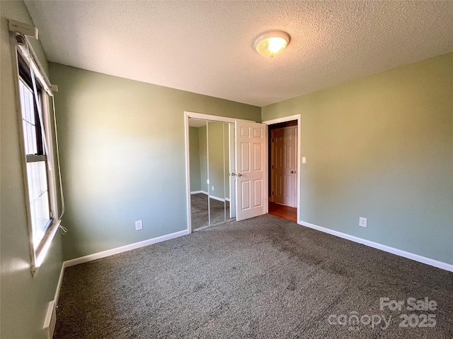 unfurnished bedroom featuring a closet, dark carpet, a textured ceiling, and baseboards