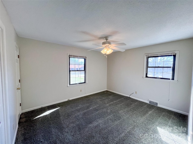 spare room featuring dark colored carpet, visible vents, a textured ceiling, and baseboards