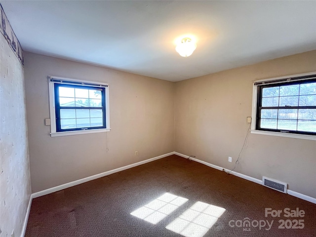 empty room with carpet floors, plenty of natural light, visible vents, and baseboards