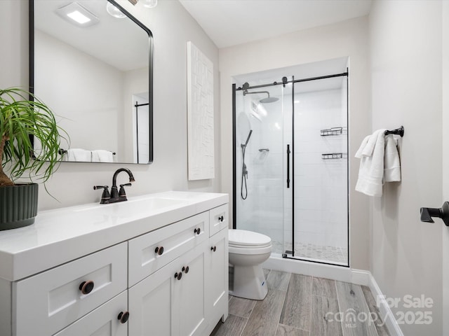 bathroom featuring toilet, a shower stall, vanity, wood finished floors, and baseboards