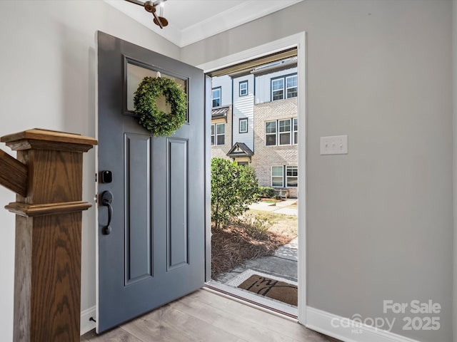 foyer featuring crown molding, light wood-style flooring, and baseboards