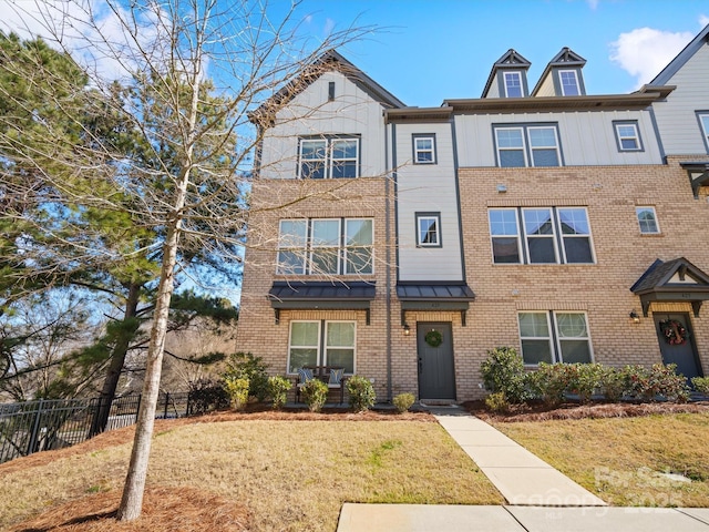 townhome / multi-family property with brick siding, a front yard, and fence