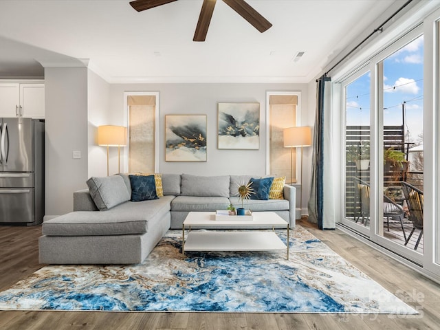 living area featuring a ceiling fan, visible vents, crown molding, and light wood-style flooring