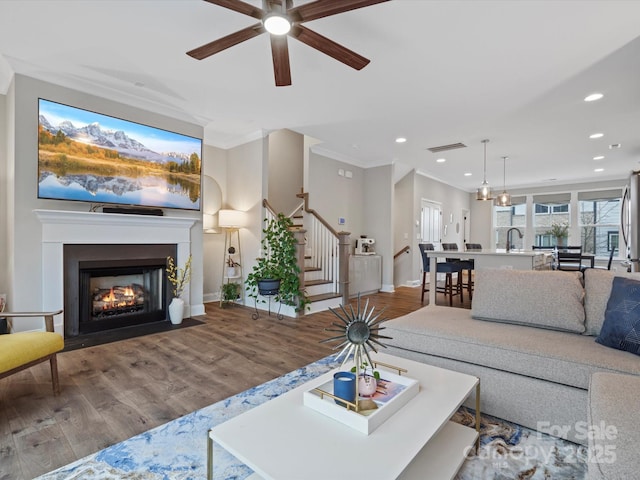 living room featuring baseboards, visible vents, ornamental molding, wood finished floors, and stairs