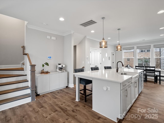 kitchen featuring a kitchen island with sink, visible vents, white cabinets, light countertops, and pendant lighting