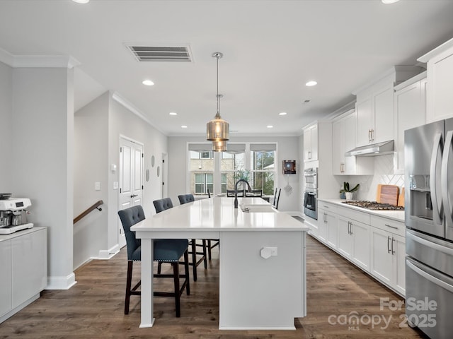 kitchen featuring stainless steel appliances, light countertops, an island with sink, a kitchen bar, and pendant lighting