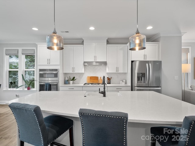 kitchen with stainless steel appliances, light countertops, decorative light fixtures, and under cabinet range hood