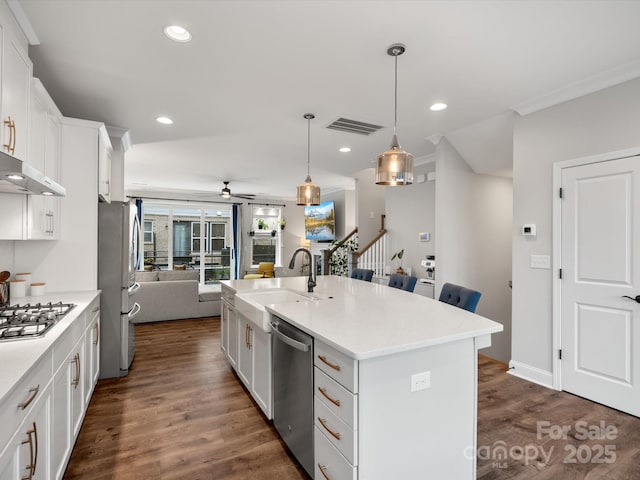 kitchen with a kitchen island with sink, a sink, open floor plan, light countertops, and appliances with stainless steel finishes