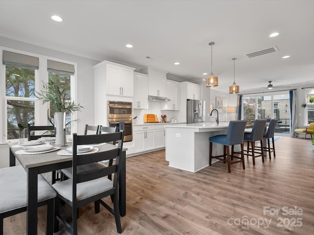 kitchen with stainless steel appliances, visible vents, white cabinetry, hanging light fixtures, and light countertops