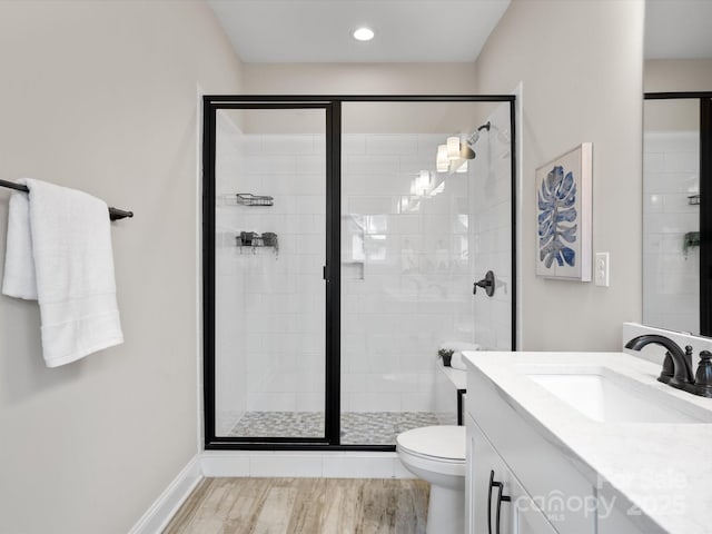 bathroom featuring toilet, wood finished floors, vanity, baseboards, and a shower stall