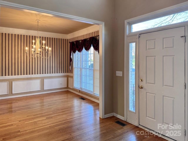 foyer featuring crown molding, wood finished floors, visible vents, and a notable chandelier