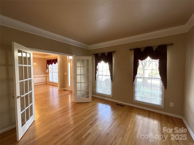 empty room featuring french doors, crown molding, visible vents, wood finished floors, and baseboards