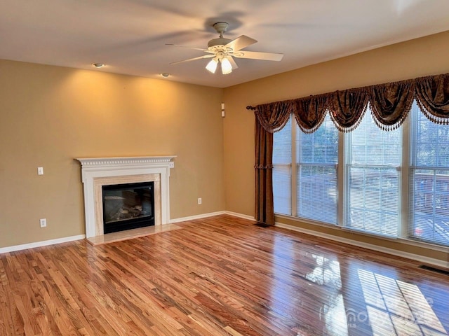 unfurnished living room featuring wood finished floors, a fireplace with flush hearth, visible vents, and baseboards