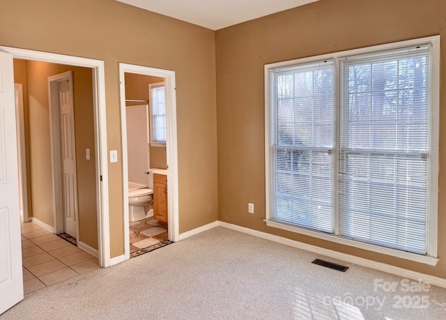 unfurnished bedroom featuring light tile patterned floors, light colored carpet, visible vents, baseboards, and ensuite bath