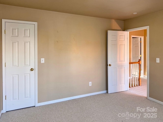 spare room featuring light colored carpet and baseboards