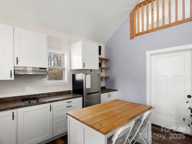 kitchen with vaulted ceiling, a center island, white cabinetry, black stovetop, and stainless steel refrigerator