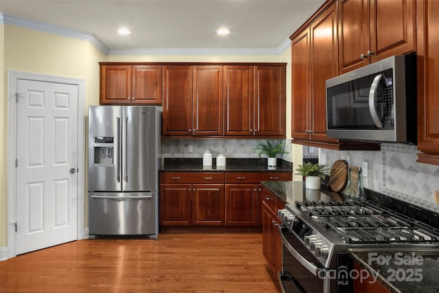 kitchen with stainless steel appliances, dark wood-type flooring, ornamental molding, and dark stone counters