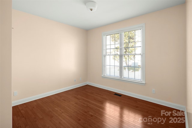 spare room with visible vents, baseboards, and dark wood-style flooring