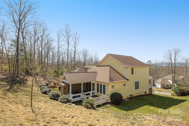 back of property with a yard, a sunroom, and a shingled roof