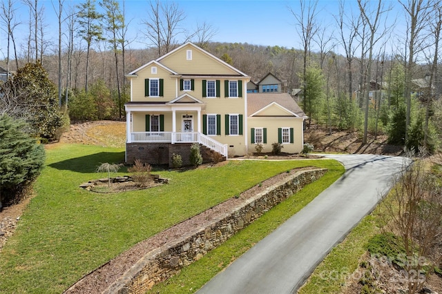 view of front of house with crawl space, covered porch, a view of trees, and a front yard