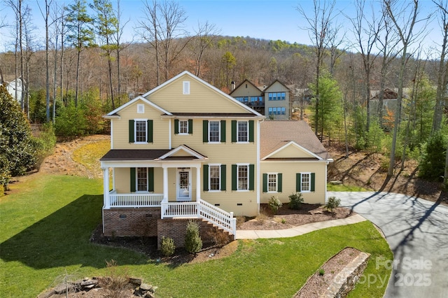 view of front facade featuring a wooded view, a shingled roof, a porch, a front yard, and crawl space