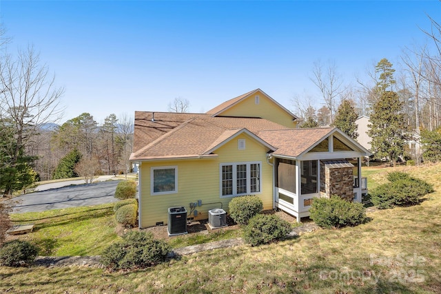 back of house featuring cooling unit, a yard, a shingled roof, and a sunroom