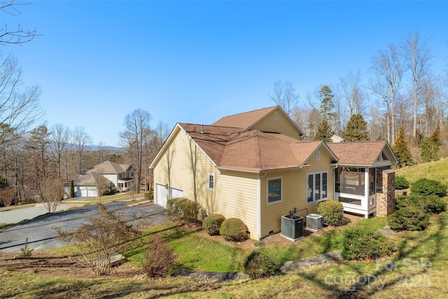 view of side of home with a garage, roof with shingles, central AC, and a sunroom