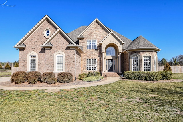 view of front facade with brick siding, a shingled roof, fence, and a front yard