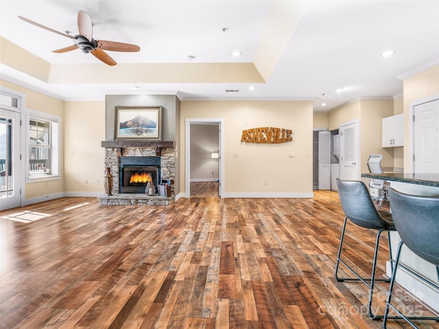 unfurnished living room with baseboards, a raised ceiling, ornamental molding, light wood-type flooring, and a fireplace