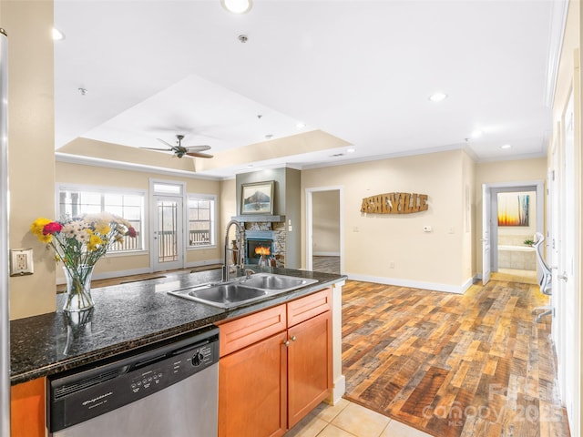 kitchen featuring dark stone counters, a fireplace, a sink, open floor plan, and dishwasher